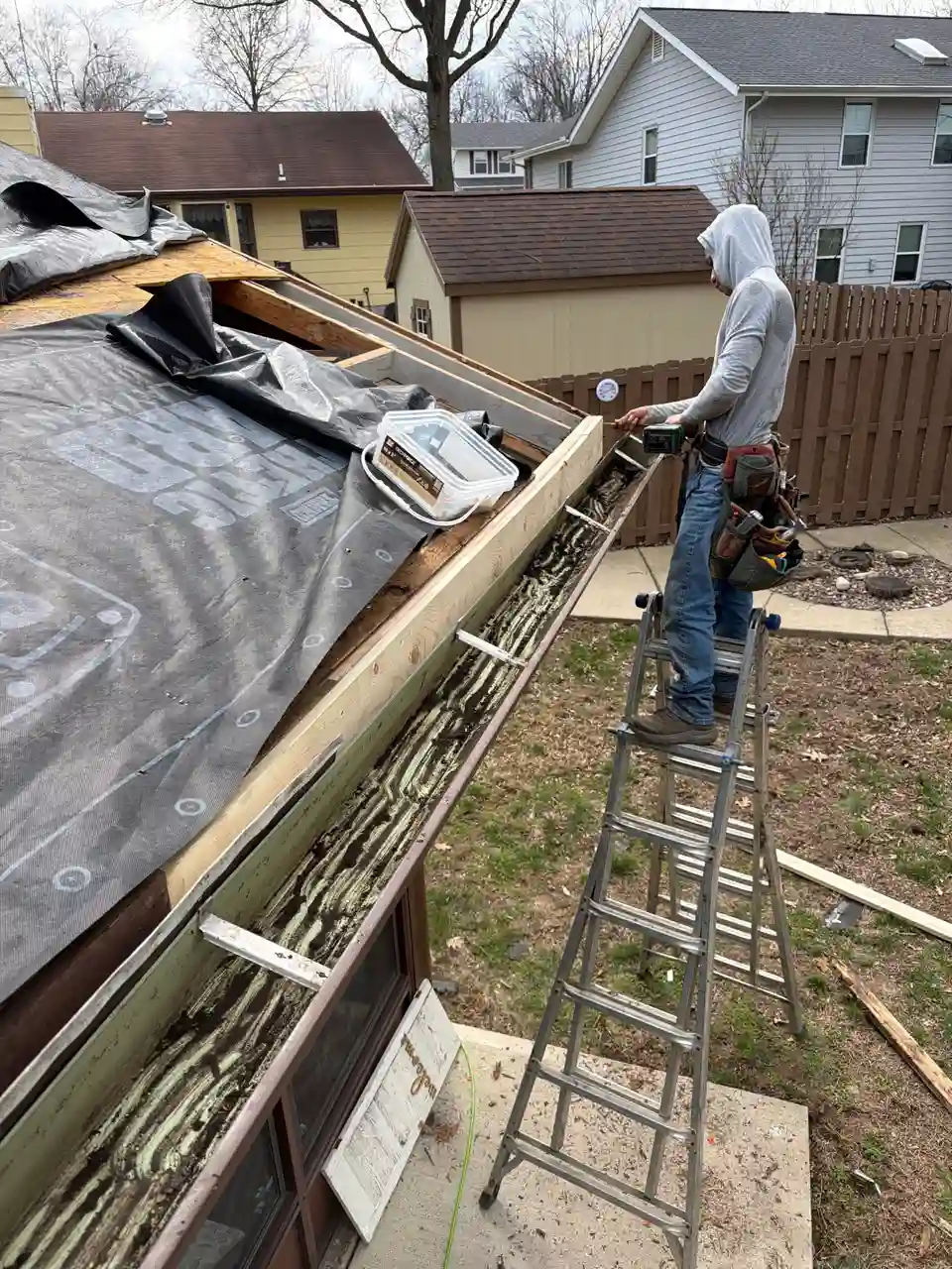 Contractor on a ladder servicing a residential gutter system on a Missouri home